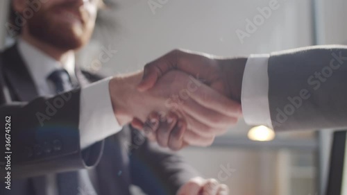 Close up selective focus shot of handshake of two multiethnic business partners in formalwear during meeting in the office