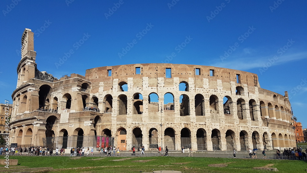 Ancient colosseum panorama with blue sky and beautiful weather, an oval amphitheatre in the centre of the city of Rome, Italy, Europe