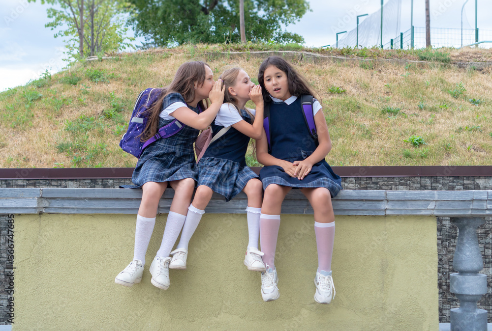 Three schoolgirls are sitting in the schoolyard. The problem of adaptation and communication at school