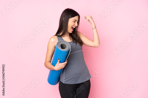 Young caucasian woman with mat isolated on pink background celebrating a victory
