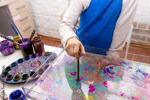 Ebru - Traditional art of origin from Turkey. The process of transferring an image to a sheet of paper. A 6-year-old girl is painting in the workshop. Close up hand with a tool.