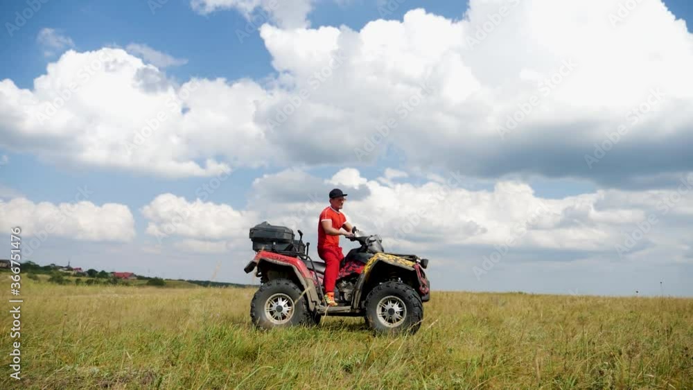 man in a black cap and red t-shirt on a colored ATV rides on a green mountain hill in summer man in a black cap and red t-shirt on a colored ATV rides on a green mountain hill in summer
