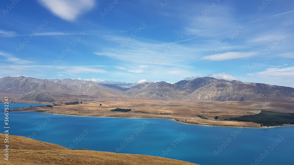 lake Tekapo with mountains view, blue sky and white clouds in summer, with a small town (township) at the southern end of the lake, South Island, New Zealand