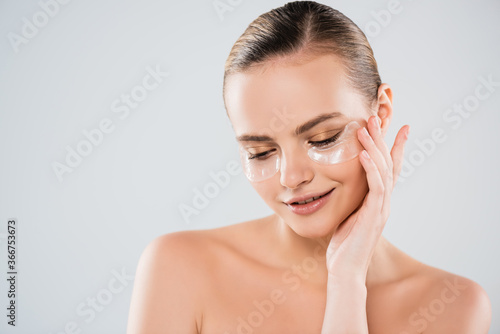 attractive and cheerful woman touching eye patch isolated on grey