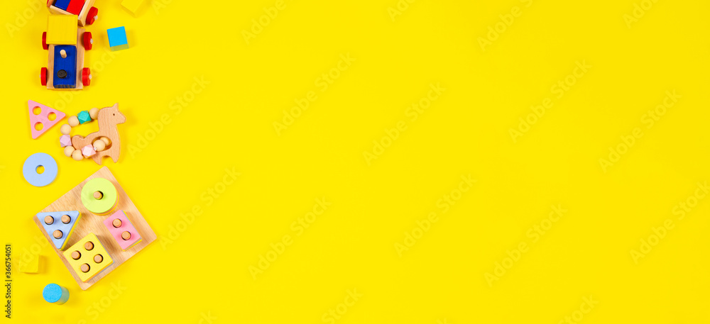 Baby kids toys banner background. Wooden train, educational stacking color recognition puzzle toy and colorful blocks on yellow background. Top view Baby kids toys banner background. Wooden train, educational stacking color recognition puzzle toy and colorful blocks on yellow background. Top view