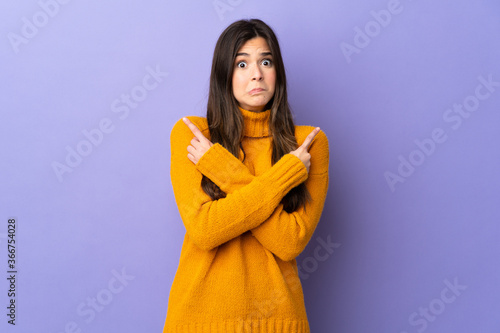Teenager Brazilian girl over isolated purple background pointing to the laterals having doubts