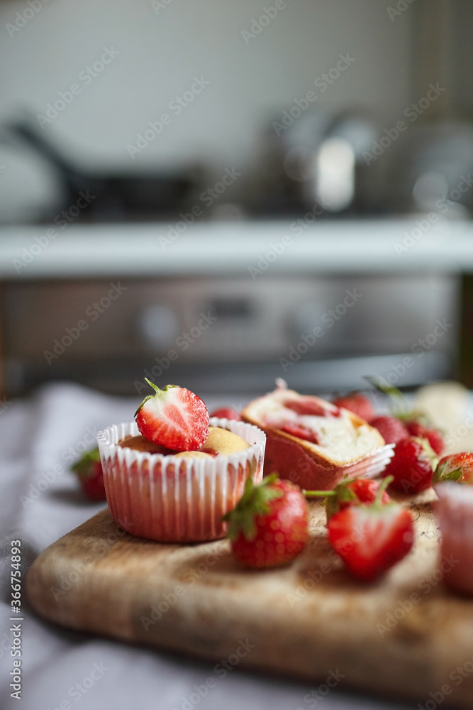 Strawberry muffins with fresh ripe berries on wooden board over kitchen table background Strawberry muffins with fresh ripe berries on wooden board over kitchen table background