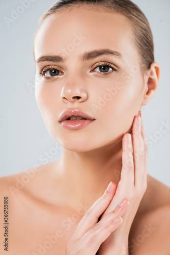 attractive and naked woman looking at camera while touching face isolated on grey