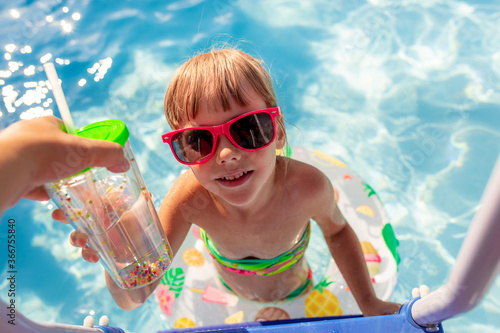 The child climbs the stairs of the swimming pool and reaches for a glass of water. Summer holidays, vacations, swimming.