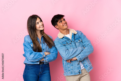 Young couple over isolated pink background looking up while smiling