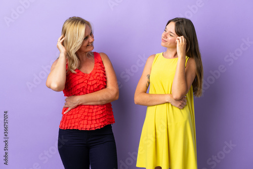 Mom and daughter isolated on purple background having doubts while scratching head
