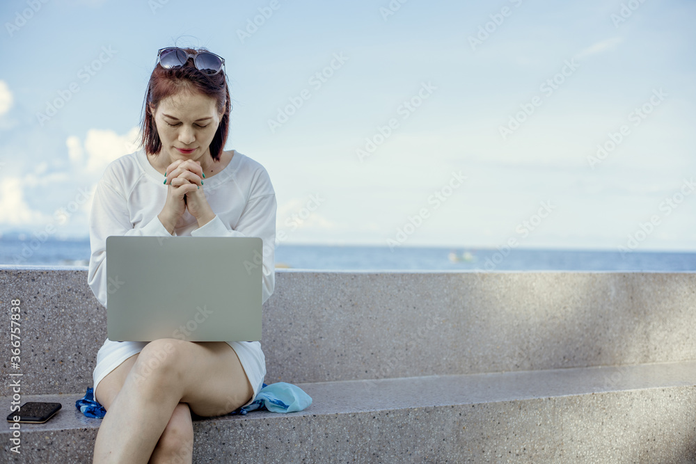 Asian female praying to god in front of a laptop working outdoor.