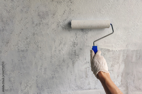 A girl paints a wall with white paint hand with roller for painting close up with copy space