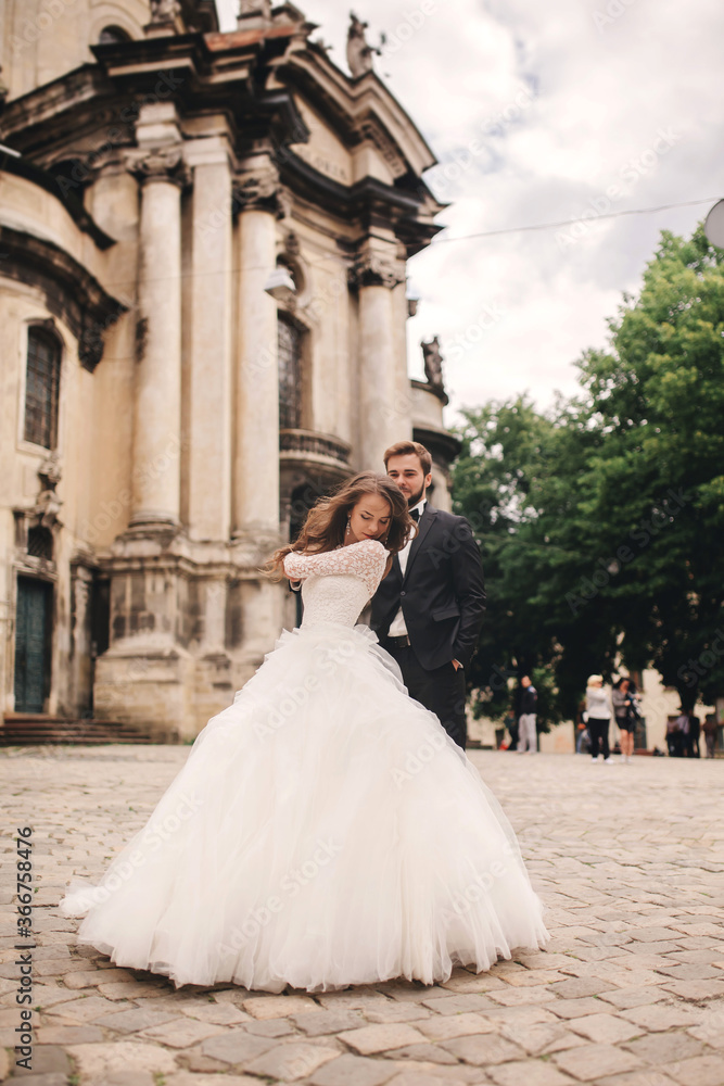 Obraz premium Stylish bride and groom gently hugging on european city street. Gorgeous wedding couple of newlyweds embracing near ancient building. romantic sensual moment of newlyweds