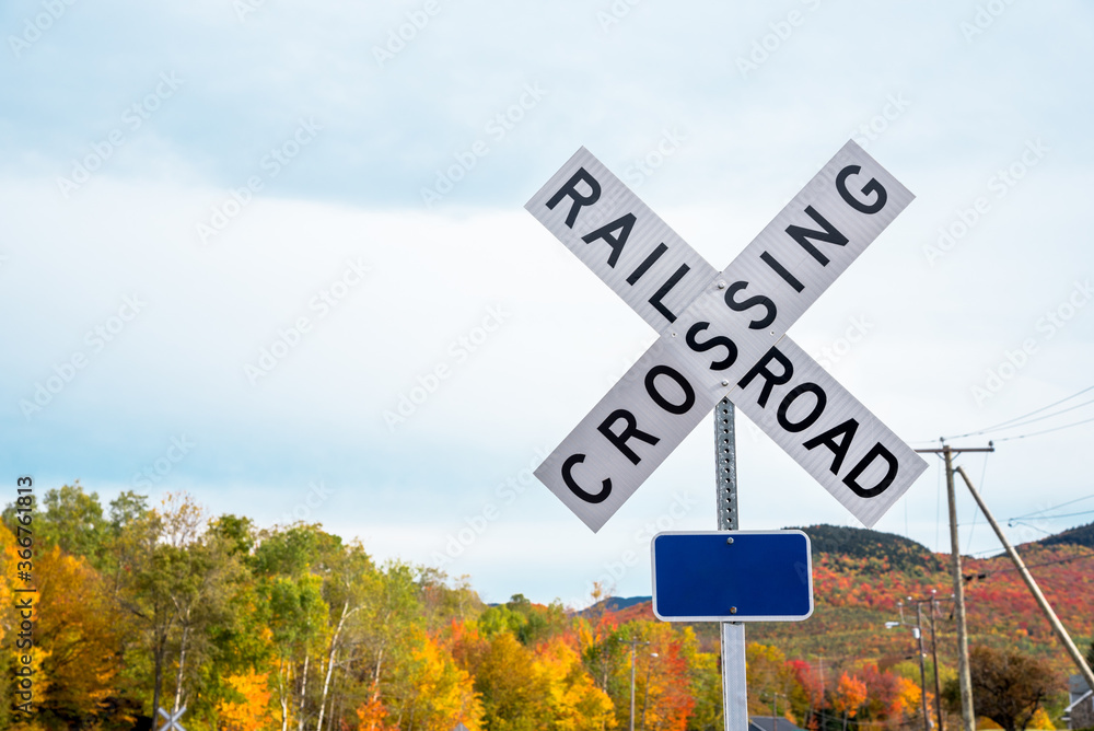Railroad crossing sign in the countryside on a cloudy autumn day. Colouful autumn trees are visible in background. Copy space.