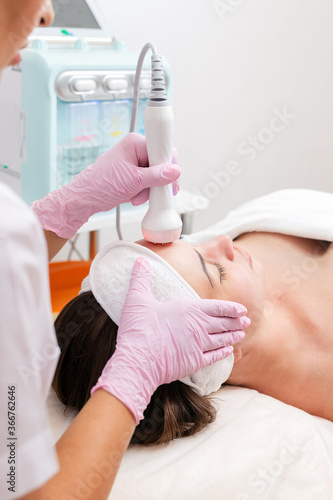The cosmetologist makes the RF-lifting procedure for the client. View over the doctor's shoulder. Vertical. Concept of cosmetology and treatment
