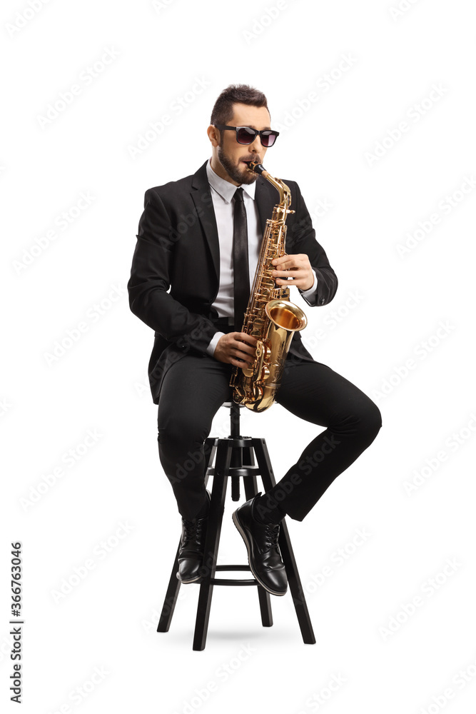 Naklejka premium Handsome man in a black suit playing a saxophone and sitting on a chair