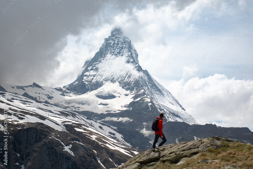 Scenic view of young trekking man looking towards Matterhorn mountain covered in clouds in the Swiss Alps
