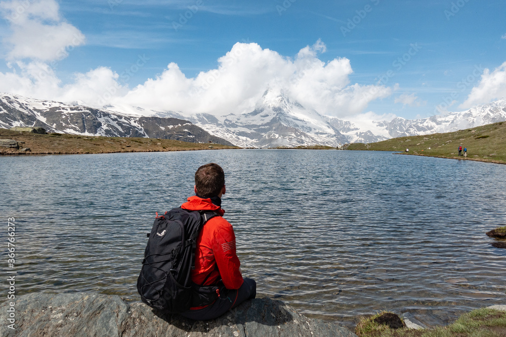 Young trekking man looking towards Matterhorn mountain covered in clouds with a lake