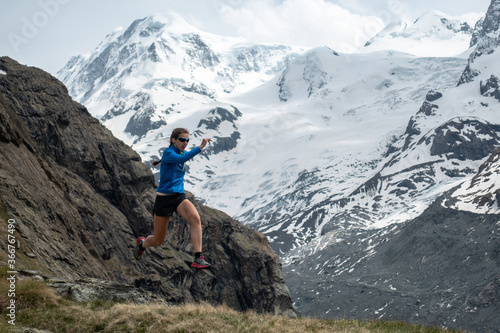 Trail runner woman jumping in alpine mountains with snow and glacier in the background