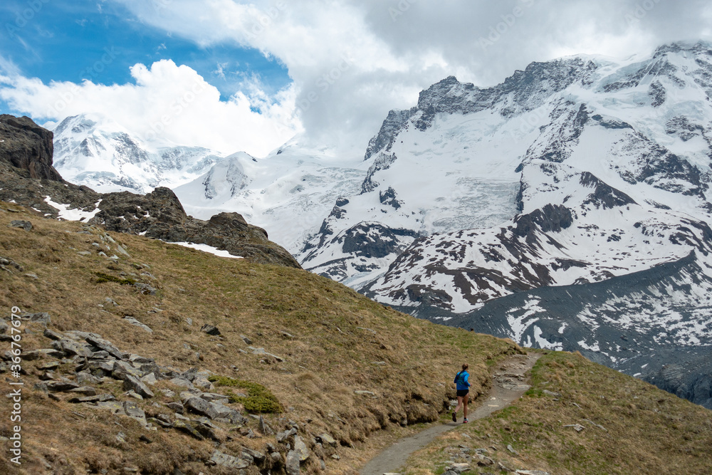 Woman trail runner in alpine mountains with snow and glacier in the background