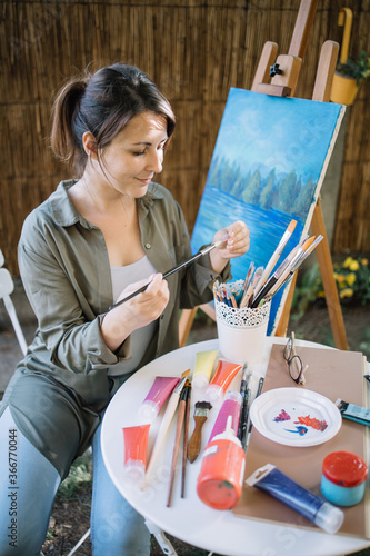 Photo Portrait of woman looking at paintbrush in garden art studio
