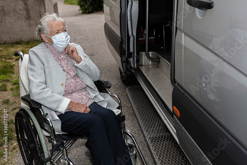 An elderly woman wearing a medical mask gets out of a disabled car.
the concept of transporting patients in the car.