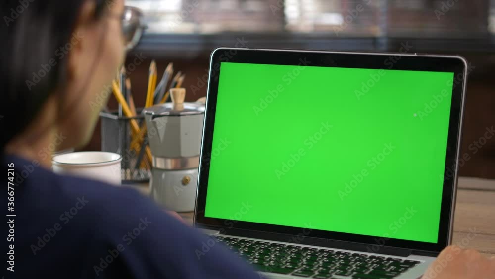​4K Dolly short. Over the shoulder shot of a business woman working in office interior on pc on desk, looking at green screen. Office person using laptop computer with laptop green screen,