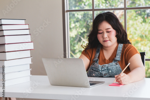 Asian fat woman with laptop computer and books working from home photo