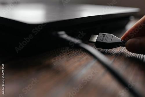 The man connects the HDMI cable to the device, inserting it into the HDMI port. Different interfaces connecting devices with each other.