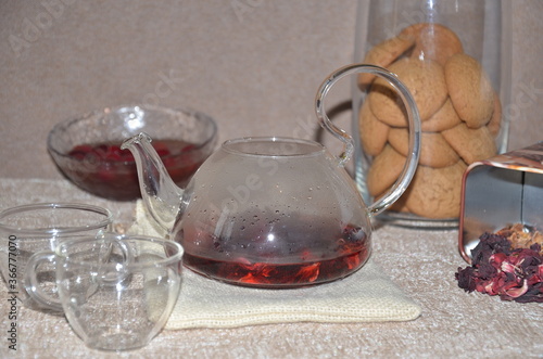 brewing process of red tea/ Serving table for breakfast, red tea in teapot. tea leaves, hibiscus and two glass cups with red tea photo