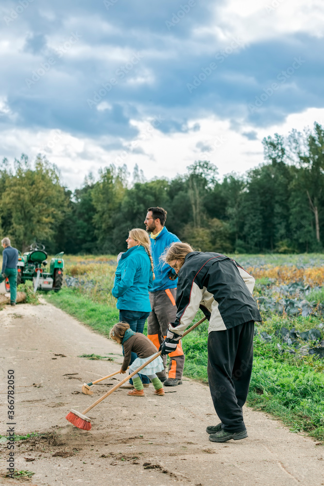 Multi-generation family sweeping footpath with brooms Multi-generation family sweeping footpath with brooms