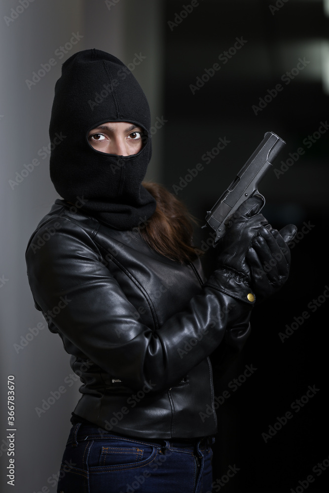 House robbery by woman in a black jacket and black mask holding black gun. Burglar in a mask. Thief in a mask trying to break into other people's apartments House robbery by woman in a black jacket and black mask holding black gun. Burglar in a mask. Thief in a mask trying to break into other people's apartments