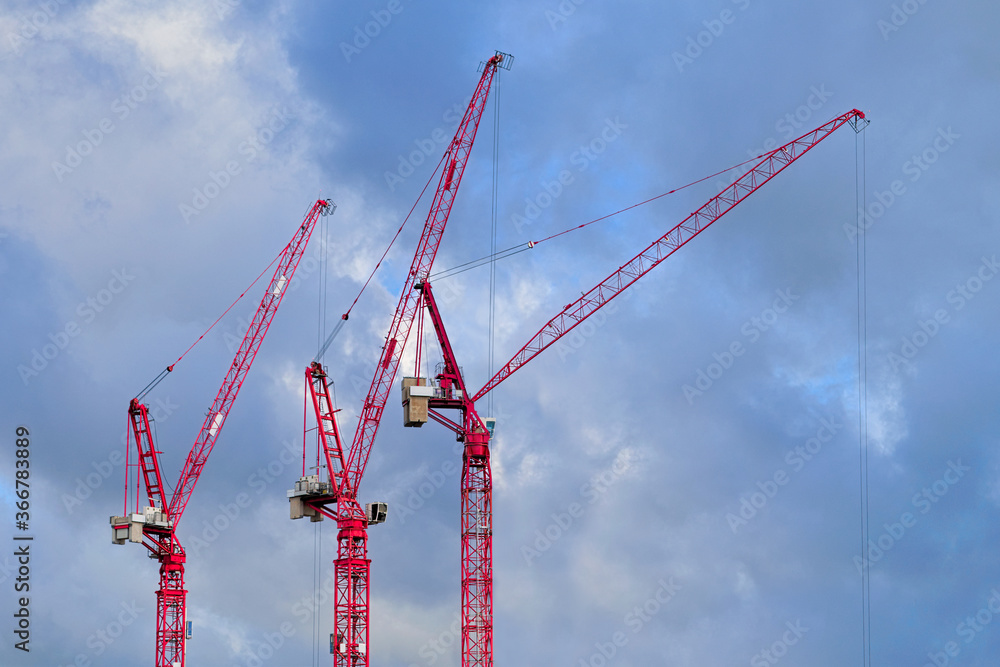 Three red tower cranes, cloudy sky background Three red tower cranes, cloudy sky background
