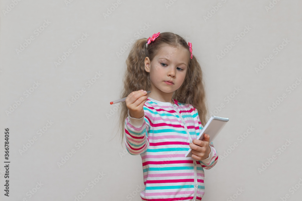 Back to school. A portrait of a fair-haired schoolgirl stands with a notebook in her hands and writes in it. Light grey Studio background. Education. copy place Back to school. A portrait of a fair-haired schoolgirl stands with a notebook in her hands and writes in it. Light grey Studio background. Education. copy place