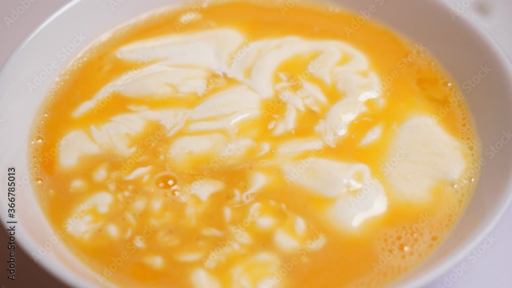 Mixing raw eggs and cream by fork in white bowl. Cooking scrambled eggs Mixing raw eggs and cream by fork in white bowl. Cooking scrambled eggs