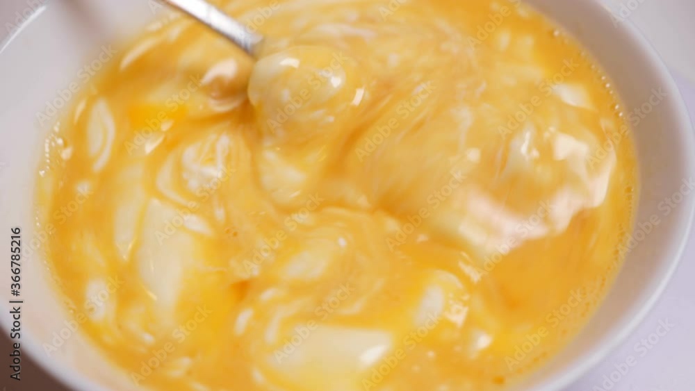 Mixing raw eggs and cream by fork in white bowl. Cooking scrambled eggs Mixing raw eggs and cream by fork in white bowl. Cooking scrambled eggs