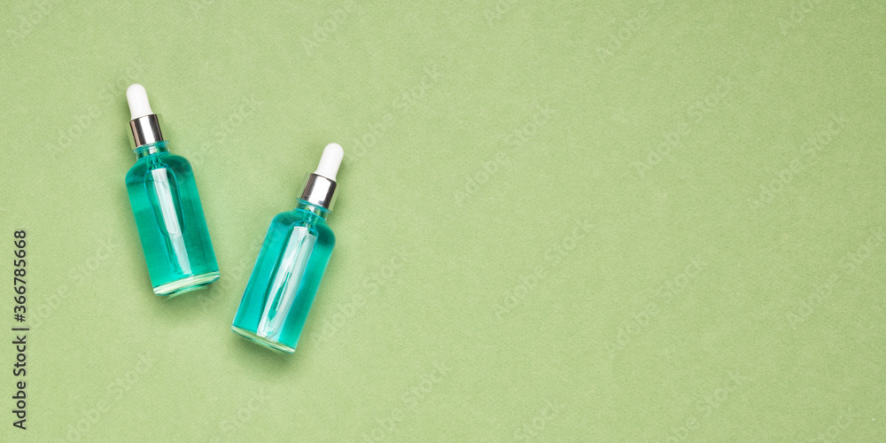 Moisturizing beauty essence or serum in a dropper glass bottle on a green background. Spa cosmetic concept, banner with copy space for your text Moisturizing beauty essence or serum in a dropper glass bottle on a green background. Spa cosmetic concept, banner with copy space for your text