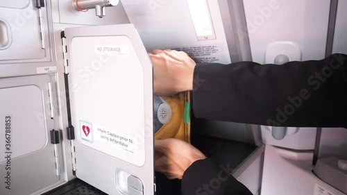 male cabin crew open galley storage and bring AED (Automated External Defibrillator) device.