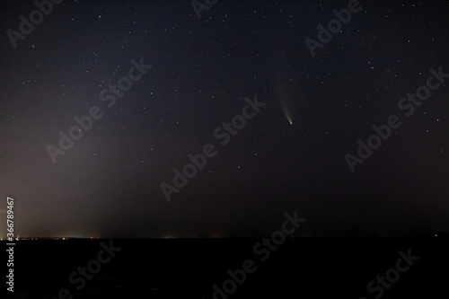 Comet NEOWISE in the dark starry sky above the horizon at night. Horizontal orientation. 