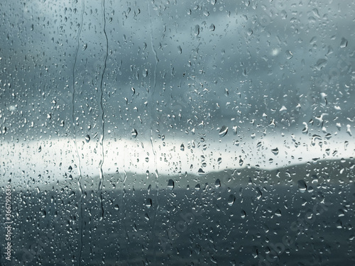 Fotografija Rainy window with heavy gray clouds and blurred mountain landscape outside