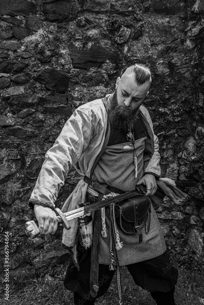 Viking warrior draws his sword in front of a stone wall