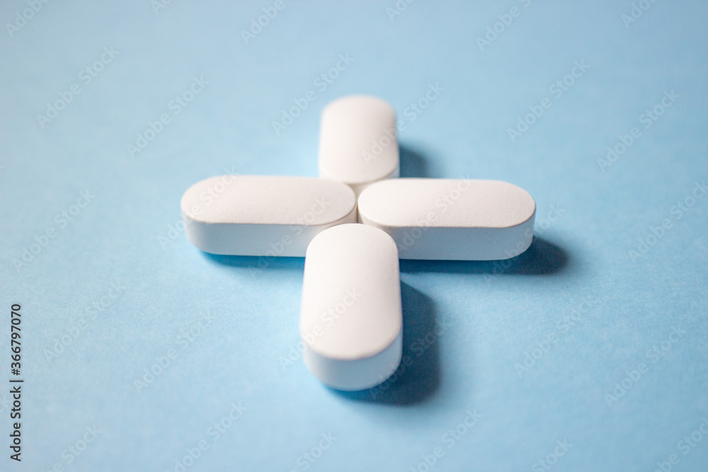 Four white pills are stacked in the form of a medical cross on a blue background, close up. Four white pills are stacked in the form of a medical cross on a blue background, close up.