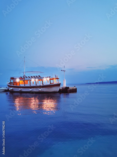 one passenger sea boat on the pier on a summer evening against the background of the blue sea and blue sky.travel.waterscape.vertical orientation.Trend of the year classic blue.