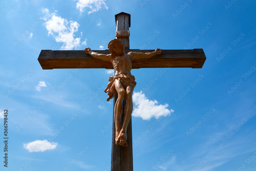 Jesus figure ( cruci fixus ) on brown wooden cross, blue sky with white clouds. Germany. Jesus figure ( cruci fixus ) on brown wooden cross, blue sky with white clouds. Germany.