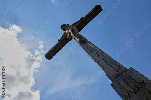 Jesus figure ( cruci fixus ) on brown wooden cross. Picture was taken diagonally from below. Blue sky with white clouds. Germany. photo