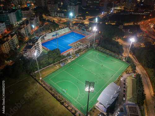 Aerial bird’s eye view of the outdoor hockey field at night. The image contains soft-focus, grain, and noise.