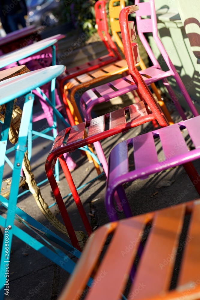 Brightly coloured metal tables and chairs outside a cafe in the sunshine,