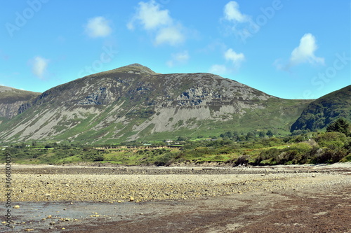 Fototapeta Naklejka Na Ścianę i Meble -  Beautiful, distant mountains at the Welsh seaside.  The shingle  beach at the small seaside village of Trefor on the Llyn Peninsula, north Wales.  A landscape with natural beauty on a summers day.