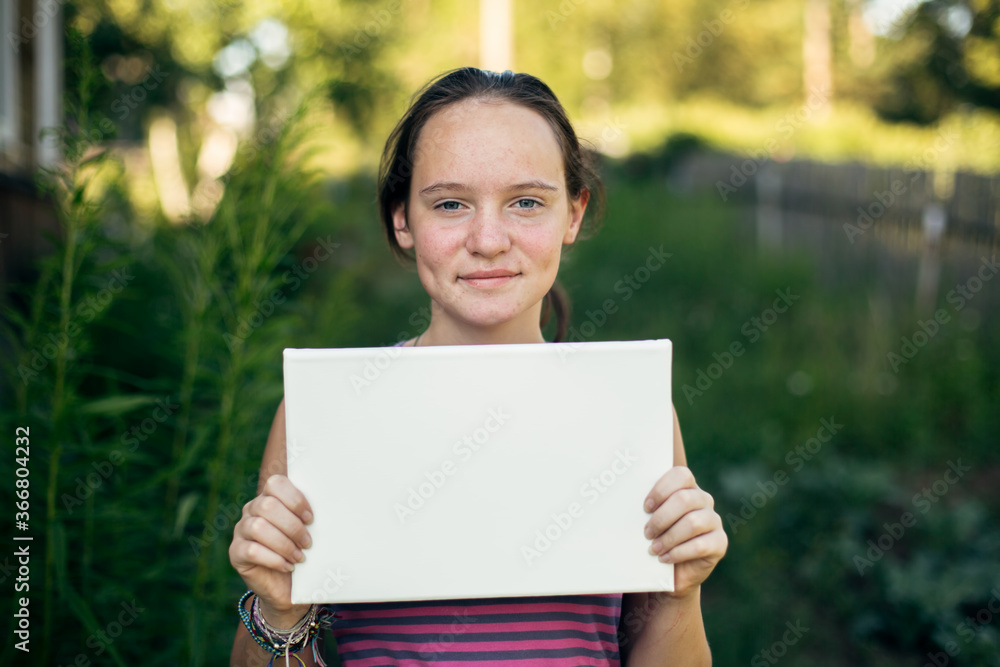 Teen girl holding clean white sheet paper (banner for message) Teen girl holding clean white sheet paper (banner for message)